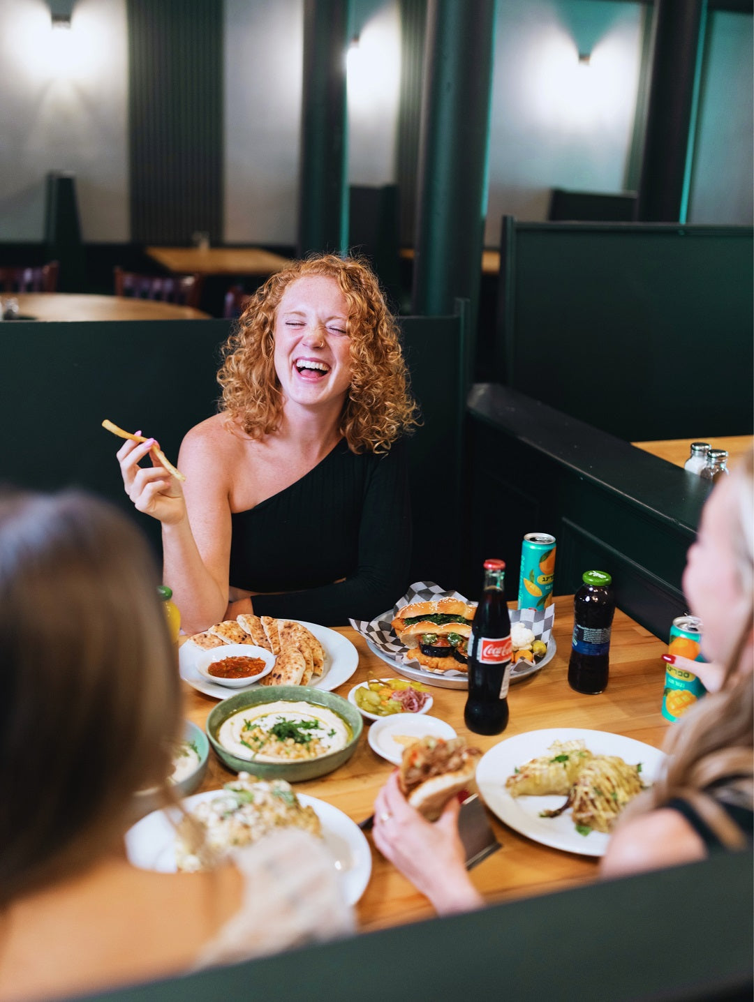 Guests enjoying Middle Eastern street food at Mazal Shawarma & Grill, with hummus plates, pita sandwiches, salads, and drinks in a warm, relaxed restaurant setting.