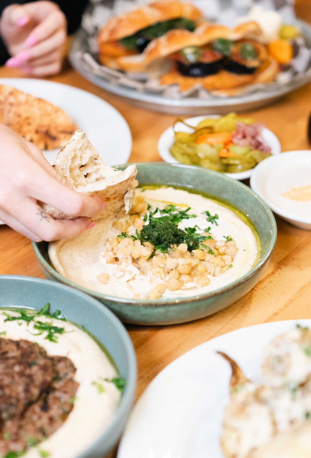 Close up of fresh pita dipping into creamy hummus at Mazal Shawarma & Grill, surrounded by additional Middle Eastern dishes and salads.